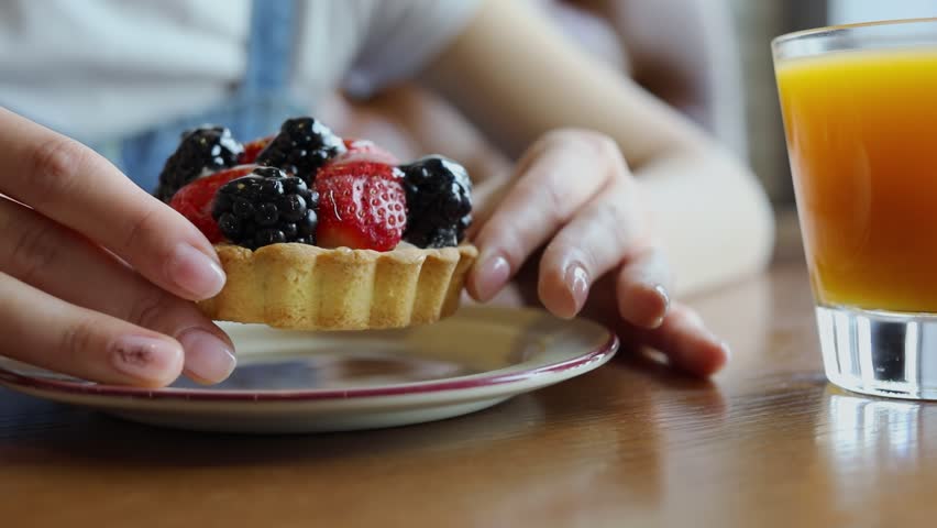 Woman holds berries cake at cafe table with cup of orange juice