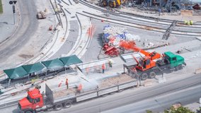Unloading and installing concrete plates from truck by crane at road construction site timelapse. Industrial workers with hardhats and uniform. Aerial top view. Reconstruction of tram tracks on - Powered by Shutterstock - Get 15% off with code: PIKWIZARD15