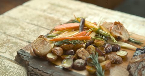 Olive oil being poured on roasted potatoes, onions and carrots, with salt sprinkled on roasted rack of pork. Medium shot in 4K Phantom Flex camera.