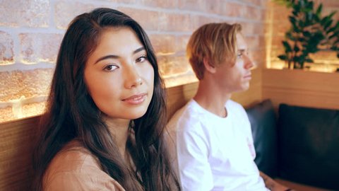 Asian girl looks at camera laughing while sitting with millennial friend waiting in restaurant in Australia during the day. Medium to closeup shot with 4K RED camera.