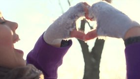 Winter girl showing heart sign and smiling. Beauty Joyful Teenage Model Girl having fun in winter park. Beautiful young woman enjoying nature and laughing outdoors. Slow motion video footage 240 fps