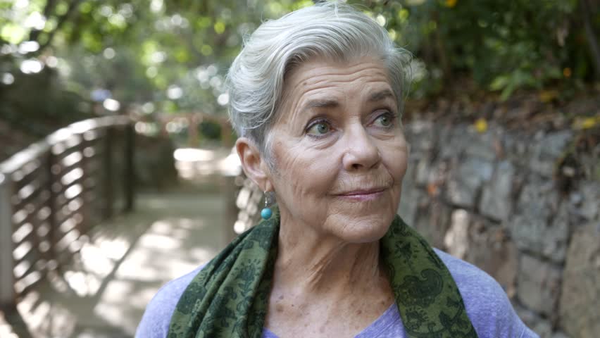 Pretty older woman takes a deep breath and looks around her surroundings at park | Shutterstock HD Video #1019201137