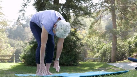 Senior citizen woman stretches and does yoga in the park on a sunny day.