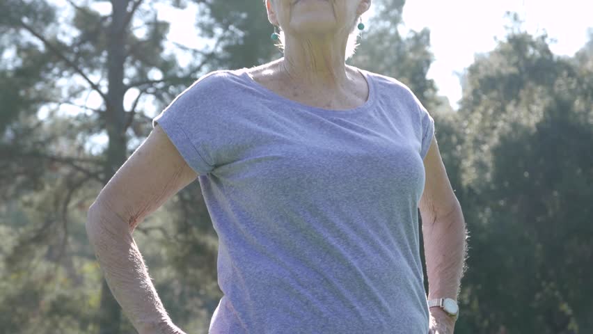 Medium shot of older woman stretching and doing yoga in the park, with a flare. Royalty-Free Stock Footage #1019201299