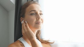 Woman sitting on window sill watching videos on smartphone and headphones
