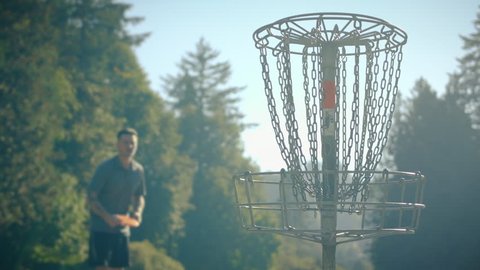 Man Throwing Disc into Basket at Frisbee Golf Course