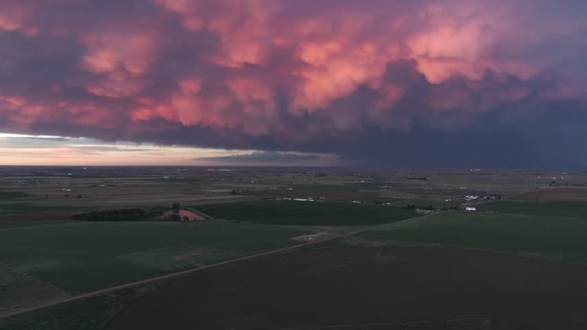 Mammatus clouds lit up at sunset over farm land in flat landscape from aerial view.