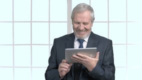 Cheerful grandfather in formal wear with tablet. Happy elderly man in business suit talking using digital tablet, window background.