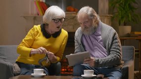 Mature couple discussing video enjoying retirement together in cozy cafe. Retired man holding tablet computer and senior woman pointing it. Slow motion.
