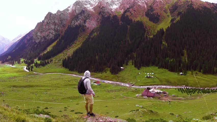 a young traveler with a backpack stands on the edge of the gorge of the mountains and looks around.