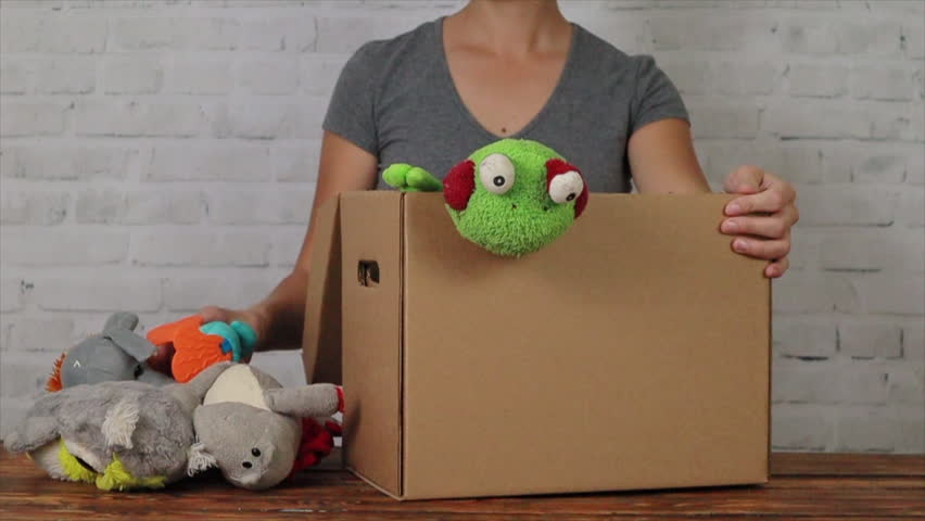 Woman volunteer is putting old toys in donation box, slow motion