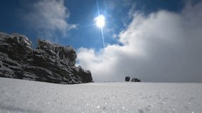 a man on a snowmobile vertically flies out of the snow boost in the mountains. against rocks and blue sky with clouds. super slow motion video with splashes and swirls of snow