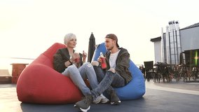 Young caucasian couple in love sitting in multi-colored armchairs on terrace in the cafe, drinking juices. Handsome guy and girlfriend talking to each other at terrace in cafe at the sunset. Outdoors - Powered by Shutterstock - Get 15% off with code: PIKWIZARD15