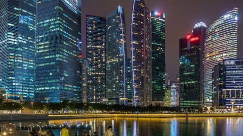 A view of Singapore business district skyscrapers in the night time with water reflections timelapse hyperlapse. Illuminated towers with blinking lights in windows