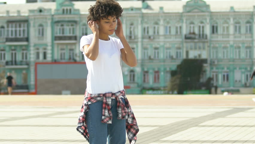 Woman putting on headphones and dancing outdoors, freedom from prejudice