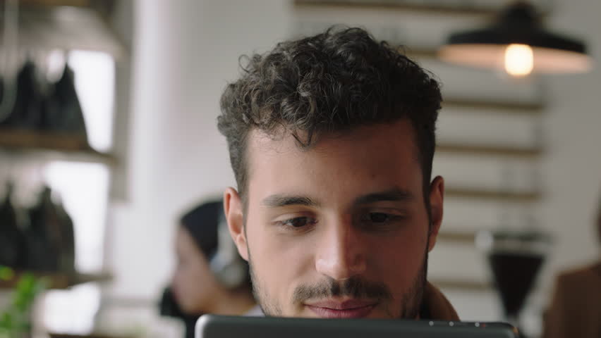 portrait attractive hispanic man using digital tablet computer in cafe drinking coffee browsing online reading social media messages on mobile device enjoying watching entertainment