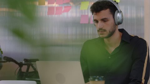 attractive young hispanic man student using laptop computer listening to music working friendly colleague sharing juice showing support in happy multi ethnic office