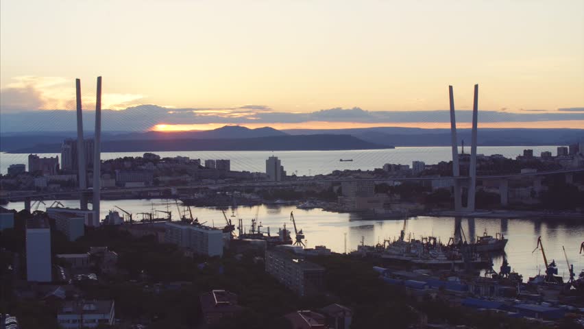 Aerial timelapse of bright sunset above the citycenter of Vladivostok, view of Golden bridge across Golden Horn bay. Russia