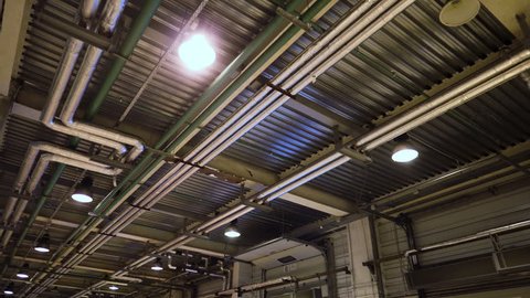 Industrial heating pipes under ceiling or another household communications pipelines in modern plant. Connections and piping with lighting on ceiling of an industrial building. Perspective. 