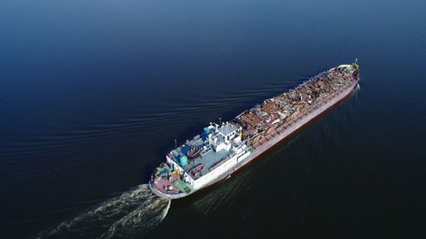 Aerial view. A barge loaded with scrap metal and waste floating on a water surface. Transportation of recyclable materials by means of a dry cargo ship.