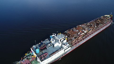 Aerial view. A barge loaded with scrap metal and waste floating on a wide river. Transportation of recyclable materials by means of a dry cargo ship.