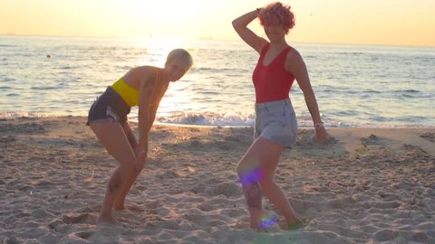 two beautiful women in red and yellow swimsuits having fun on beach during sunset or sunrise