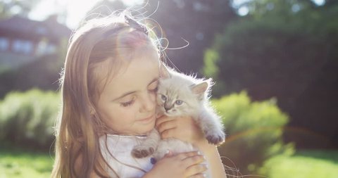 Close up of the small pretty girl standing in the park and hugging cute little fluffy cat. Portrait. Outside.
