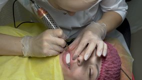 Cosmetic procedure of permanent make-up of lips. Woman-cosmetician applies the paint with a needle on the girl's lips in the beauty salon. Close up. 