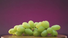 Video of a bunch of grapes rotating 360 degrees. Purple background, referring to wine.