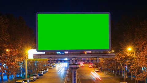 A billboard with green chroma key on a background of a city night landscape of fast moving cars with long exposure. Time Lapse video.