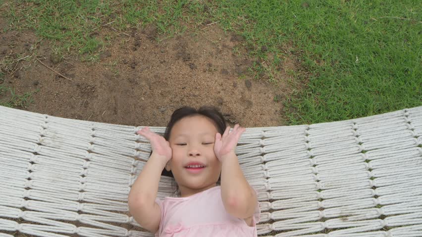 Little asian girl ralaxing on white cradle in park