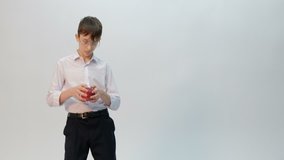 A young man is a student or a schoolboy with glasses and a white shirt with a red apple in his hands. Teen makes funny dance moves wagging her hips. Emotions. Isolated. Copy space. Unprocessed video.