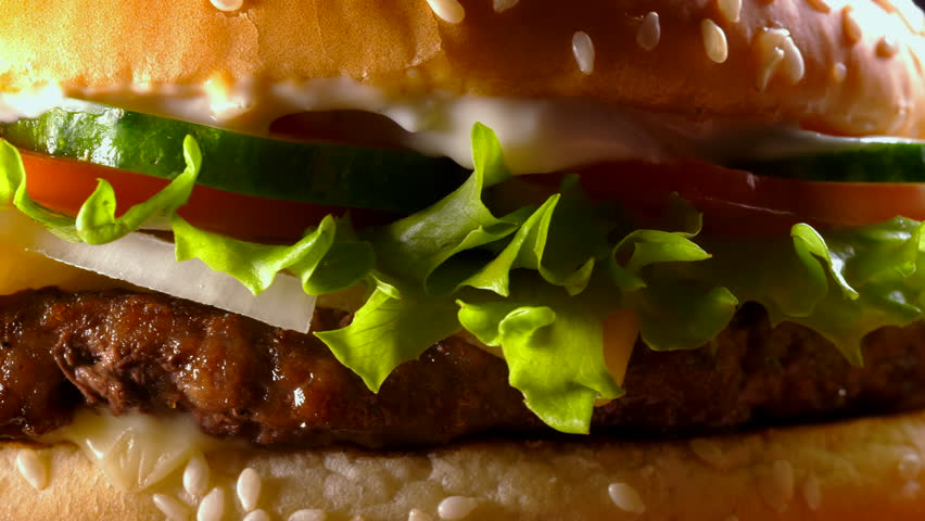 Yummy fast food concept. Fresh homemade grilled burger with meat patty, tomatoes, cucumber, lettuce, onion and sesame seeds. Unhealthy lifestyle. Food background. 4k Royalty-Free Stock Footage #1019263309
