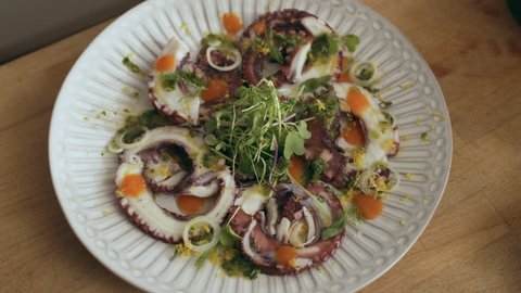 Beautifully plated octopus carpaccio dish on a cutting board. Close shot on a RED camera.