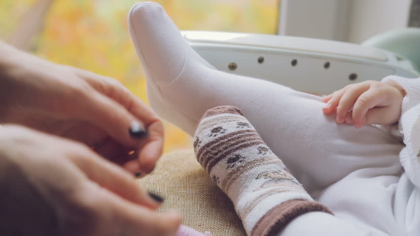 Mom puts socks on the legs of a small newborn baby.