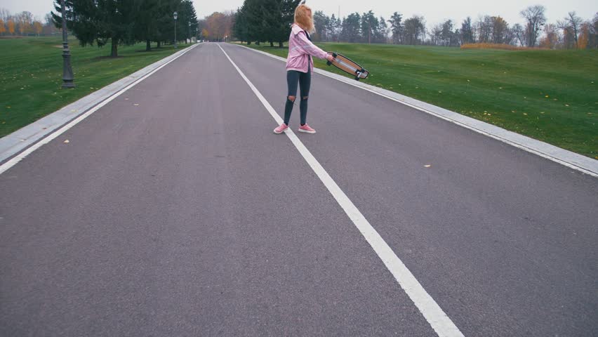 Young pretty beautiful blond hipster woman walking down the road with skateboard longboard in slow motion.