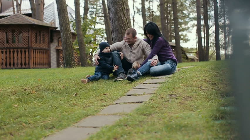 Young family relaxing in the park with his dog. Family siting on a grass