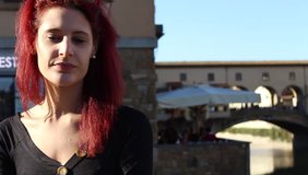 PONTE VECCHIO, FIRENZE, ITALY - November 10, 2018: Smiling girl in a beautiful sunny day in Florence; on the background the famous old bridge visited by many tourists. HD video, portrait, outdoor scen