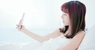 woman take a selfie by smart phone happily and sit in the bed at home