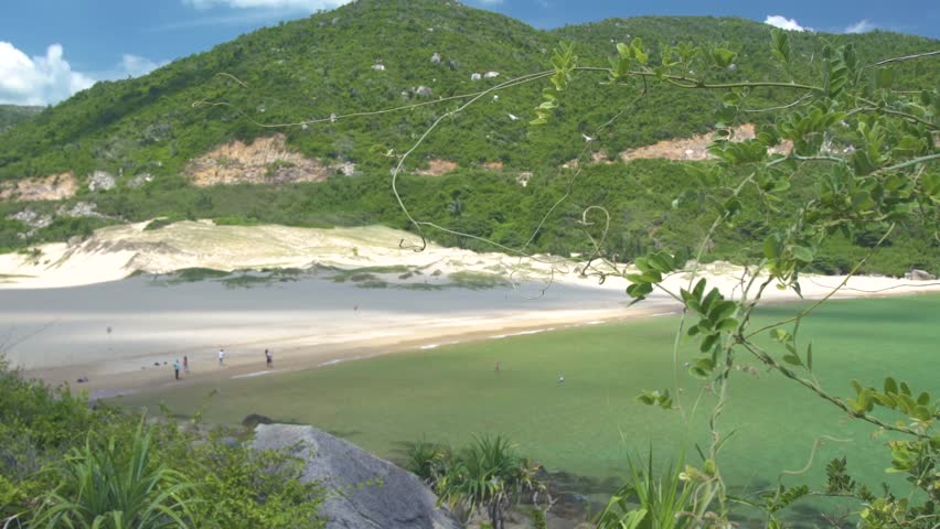 People resting on sandy summer beach and swimming in turquoise sea on green hill ladscape. Tourist people on sea beach with crystal clear water. Green highlands on tropical island
