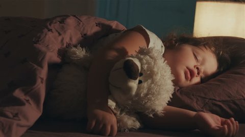Sleeping baby happy and carefree in bed hugging a teddy bear toy. Happiness in sleep, children without coughing.