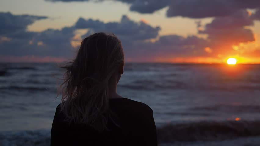 Girl relaxing in nature enjoying beautiful sunset landscape above the sea. Woman looking at ocean view at sunset thinking about life. 