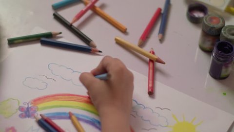 Small Child coloring a rainbow, crayons , color pencils and paints all around him