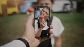 Cinemagraph of cute funny looking girl or young hipster millennial teenager woman eat ice cream or gelato, when best friend makes video for social media on smartphone. technology is fun