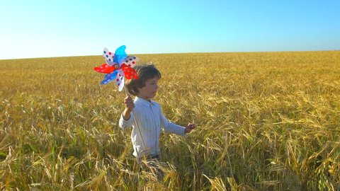 Cute little boy holding toy wind turbine in hand, running at sunset. Wheat field. Happy kid, child playing, having fun with pinwheel. Happiness, nature, vacation, childhood, children, happy family