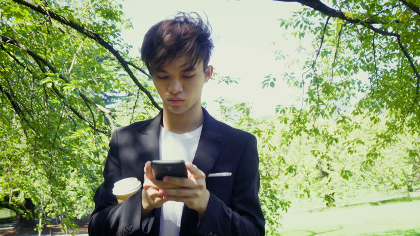 Young Asian Business Man Texting on Phone During Break in Park - Model Released