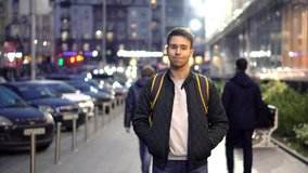 Young happy smiling man standing in the evening street with bokeh light effect. 4k Video Clip