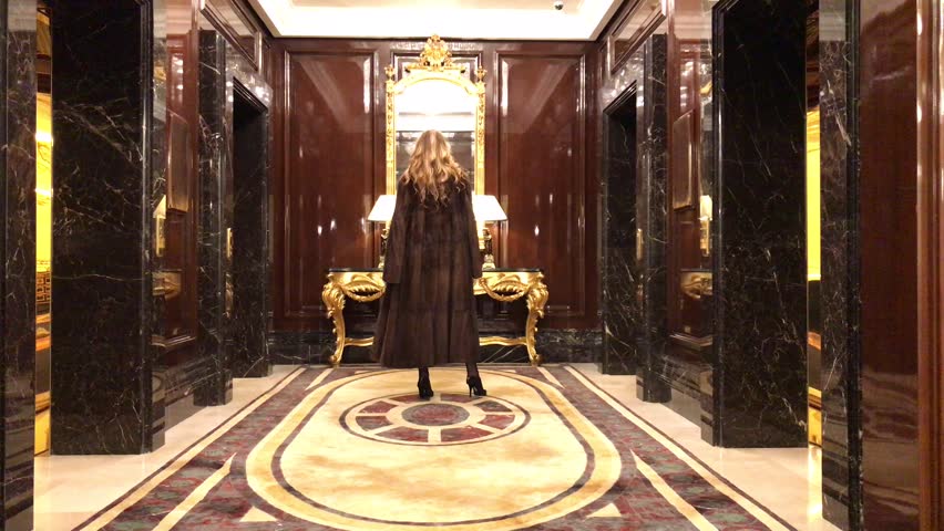Young slim blonde woman in a mink coat posing in the lobby of an expensive hotel