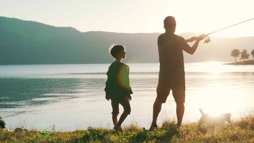 Man boy fishing, stand on shore large calm lake fish with rod slow motion slide sunset. Dad and son cast spinning into calm water surface. Lens flare Dog Jack Russell Terrier. Tourism. Go Everywhere Royalty-Free Stock Footage #1019313295