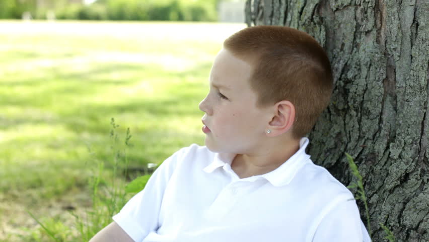 Young boy relaxing in grass against tree